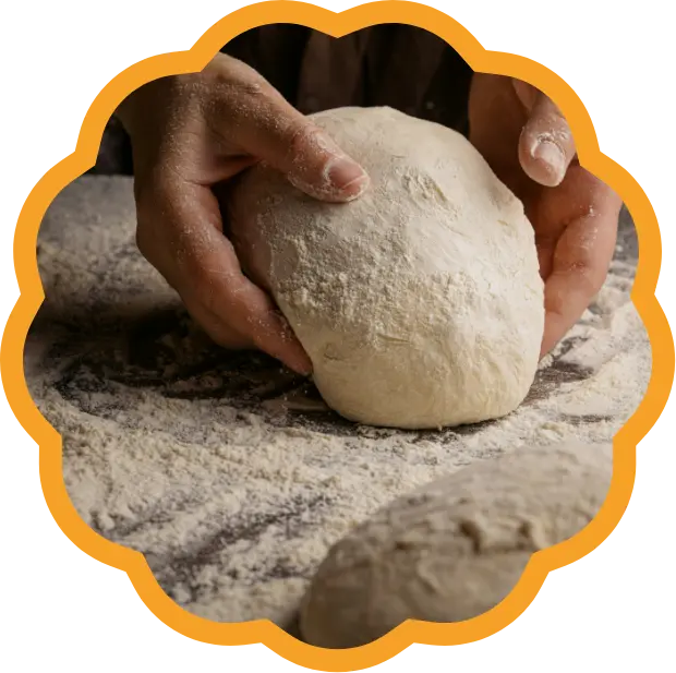 Deux mains façonnent une boule de pâte à pain sur un plan de travail fariné.